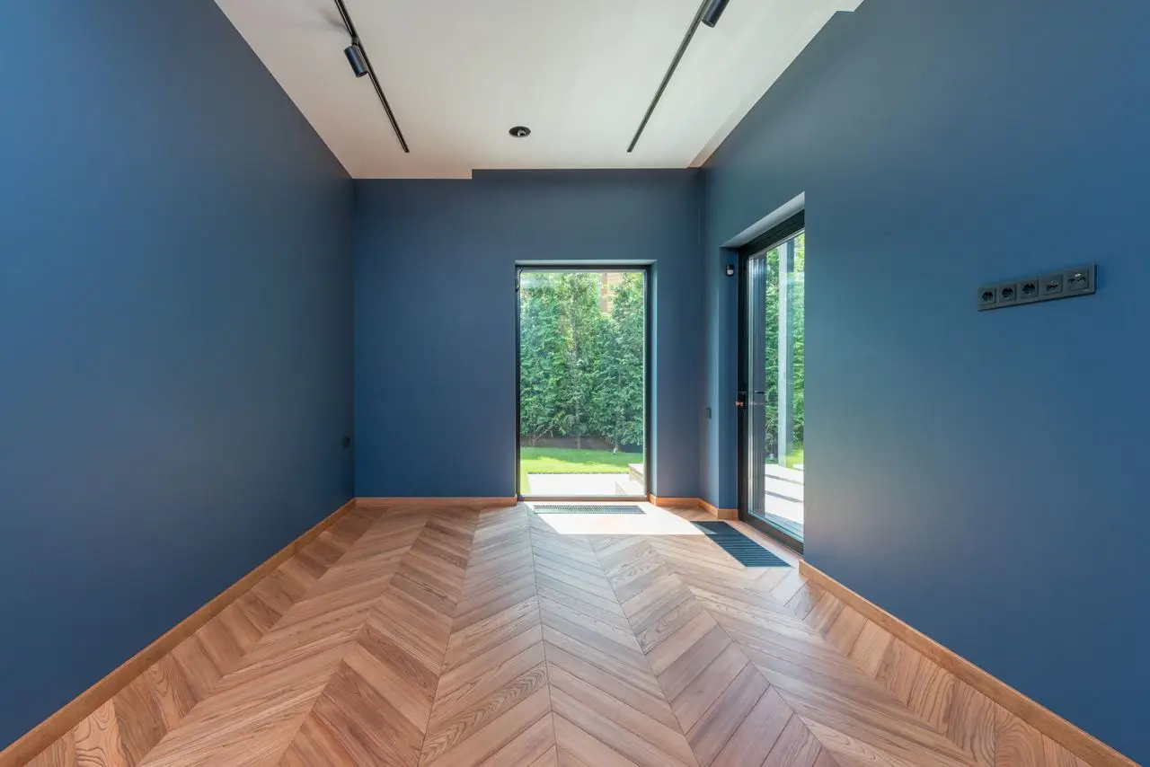 Spacious room featuring blue walls, wooden herringbone floor, and glass doors leading to a garden. Eagle, ID